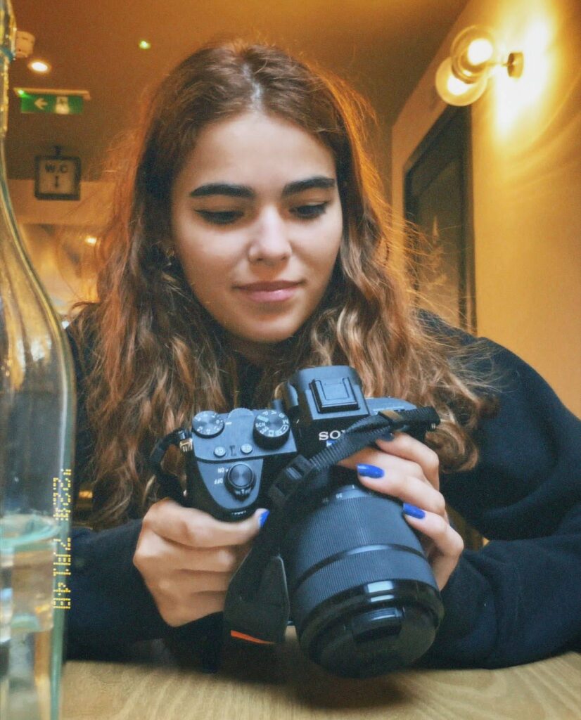 Sofia Leite, artista multimédia e produtora audiovisual, segura uma câmera enquanto trabalha em um projeto criativo.